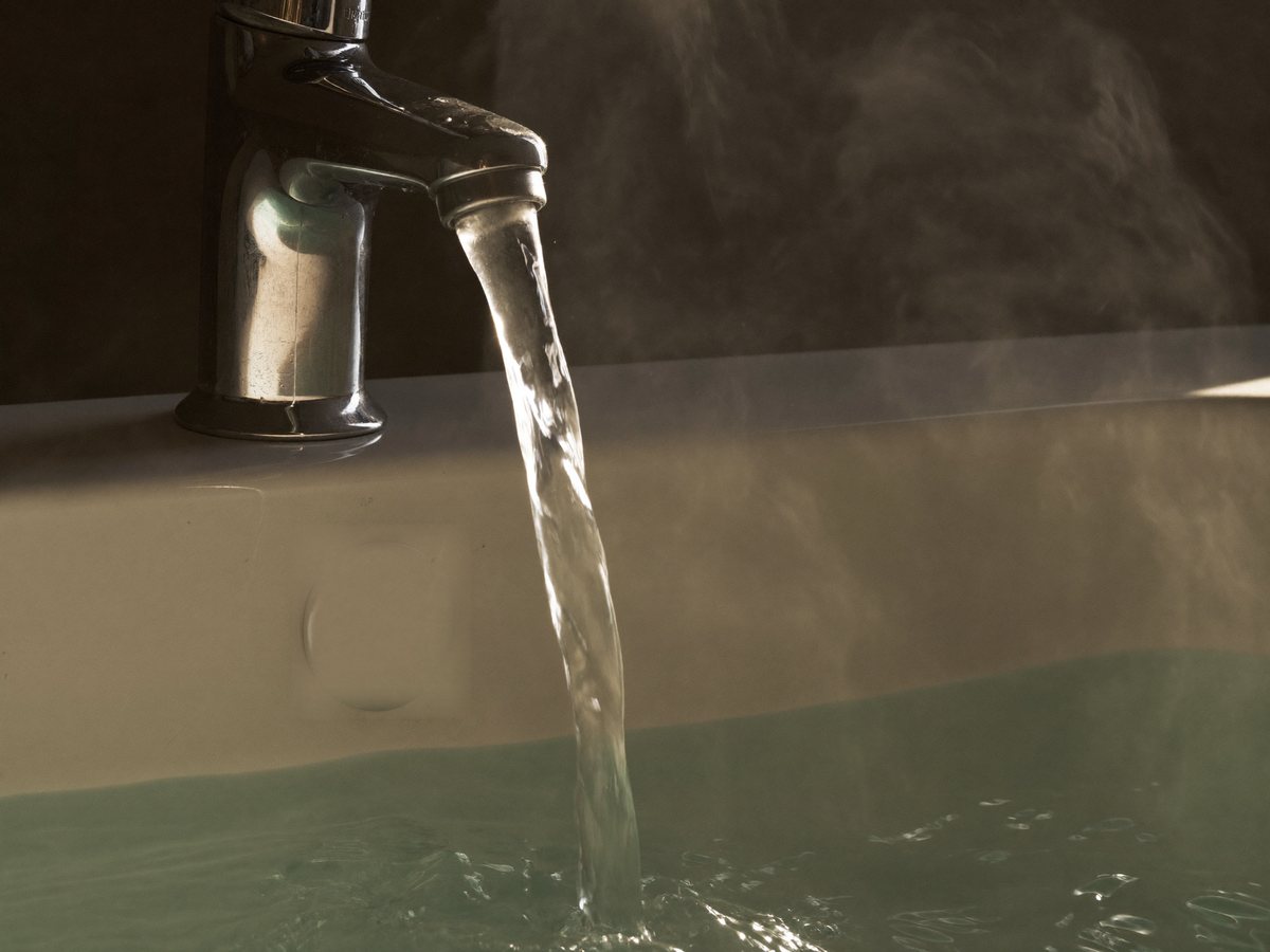 Warmes Wasser läuft aus einem Chromhahn in ein weißes Keramikbecken, darüber steigt leichter Dampf auf